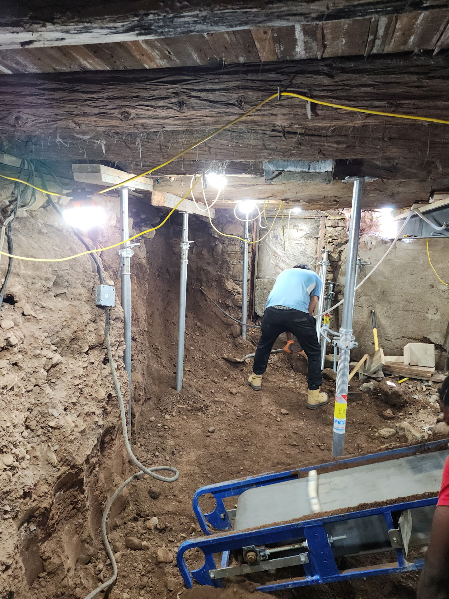 Crew member excavating a basement lowering dig with adjustable steel shoring posts